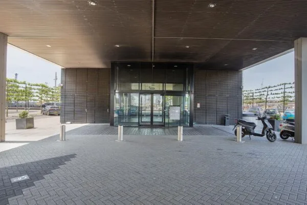 Ingang van een modern kantoorgebouw aan de Waalhaven-Oostzijde met glazen schuifdeuren, scooters en parkeergelegenheid.